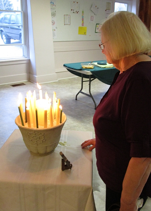 A women stands by a container of lit candles for the Celtic Prayer Service.